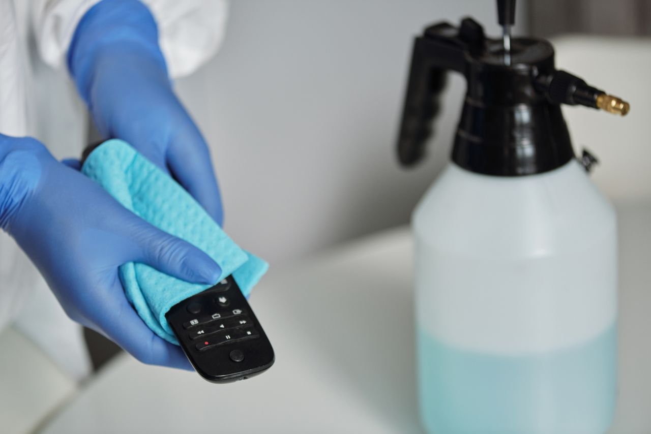 home-hero Close-up of gloved hands disinfecting a remote control with a cloth and spray bottle.